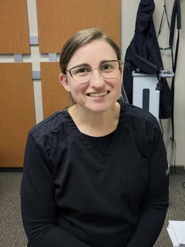 Alisa smiling, while wearing black scrubs.